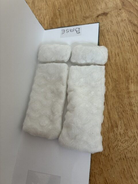Two white rectangular blankets laid side-by-side with two smaller white pillows positioned at the top, forming a simple sleeping arrangement.